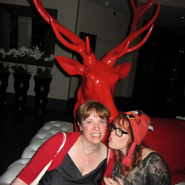 Two people sit in a chair with a red dragon statue behind them.