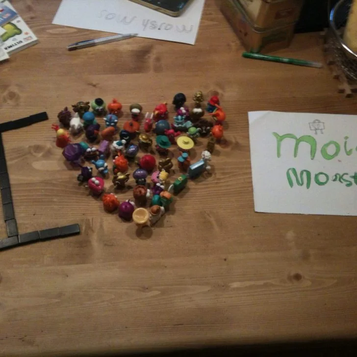 A wooden table is covered with office supplies, including a post-it note, a writing implement, and a crayon, as someone is handwriting an artistic creation.