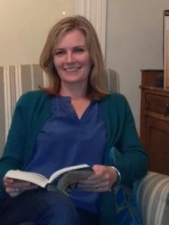 A person with a smiling face is sitting in a room surrounded by furniture, holding an adult.