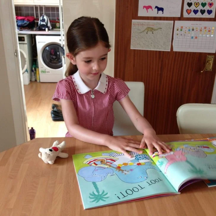 A young person and person are learning together at a table filled with furniture, books, and child art.