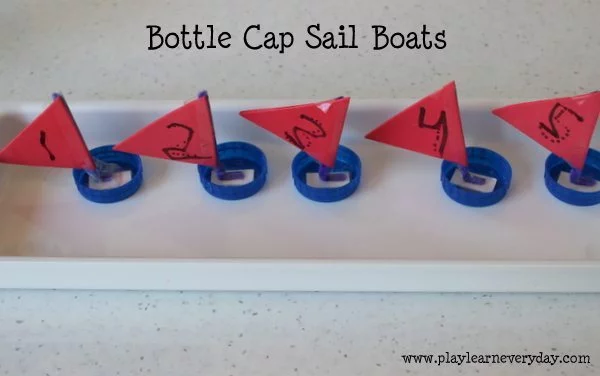 A group of carmine origami bottle cap sail boats are floating in a pool of water.