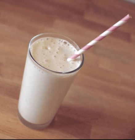 A cup of creamy malted milk, topped with a drinking straw, sits on a table indoors, ready to be enjoyed as a health shake, milkshake, soft drink, milk, irish cream, lassi, or smoothie.