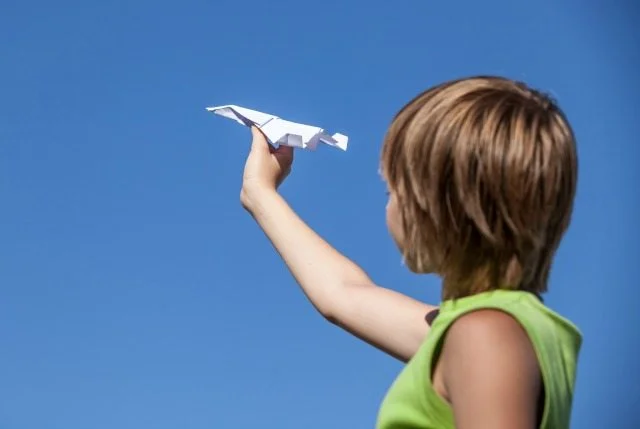 young boy with paper plane against blue sky