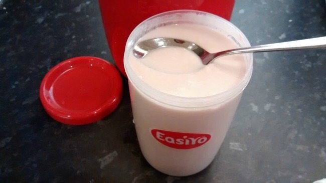 A cup of yogurt sits on a table with a spoon.