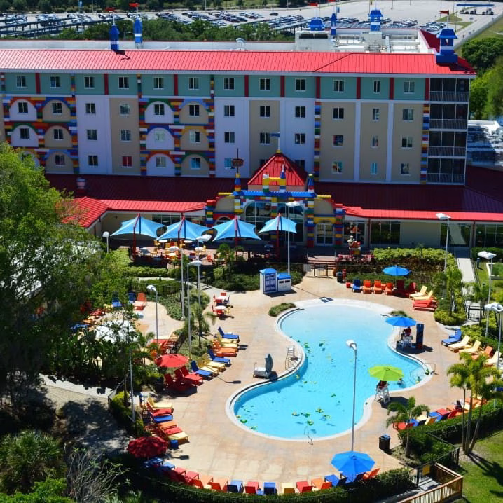A lush tree towers over a sparkling swimming pool surrounded by a resort town of buildings, hotels, and spas, providing a perfect playground for a relaxing vacation.