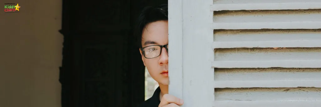 Man with glasses peeping out from behind a door.