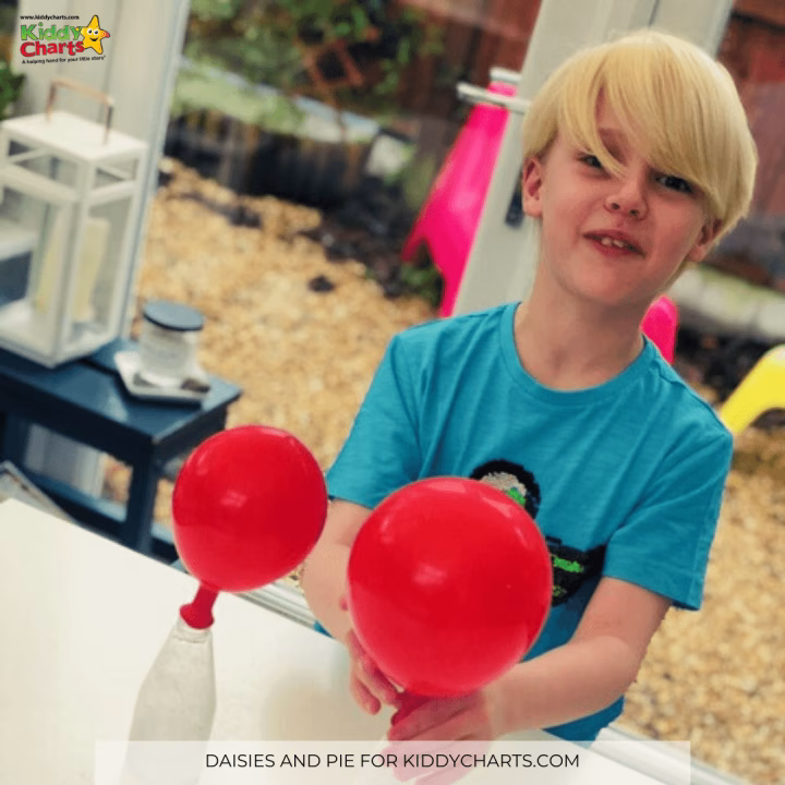 A smiling person holds a red balloon and toy amidst a backdrop of colorful party supplies indoors.