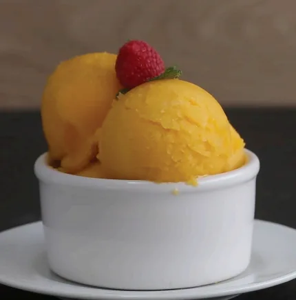A bowl of gelato topped with fresh fruit is being enjoyed indoors, providing a sweet and creamy frozen dessert.