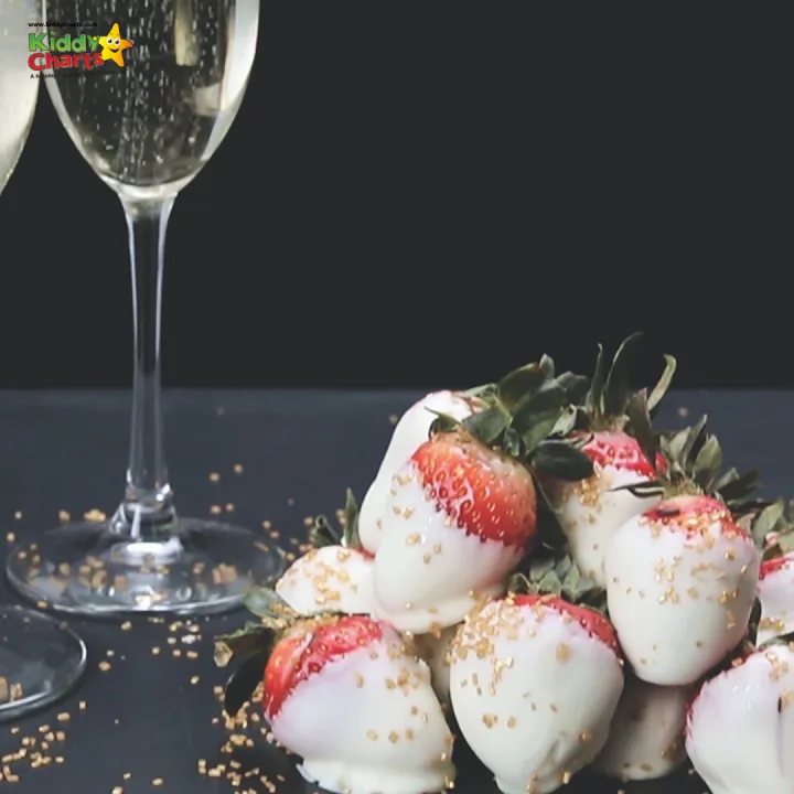 A strawberry sits atop a glass of champagne in a set of elegant stemware on a table surrounded by other wine glasses and tableware.