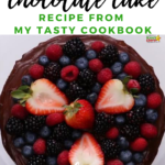 A delicious chocolate cake topped with a variety of fresh fruits, including strawberries, frutti di bosco, and alpine strawberries, in the image, showcasing a dairy-free and vegan recipe from Kiddy Charts' cookbook.