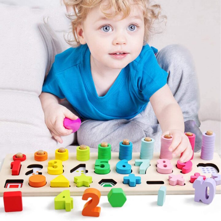 A toddler plays with baby toys while wearing baby and toddler clothing indoors.