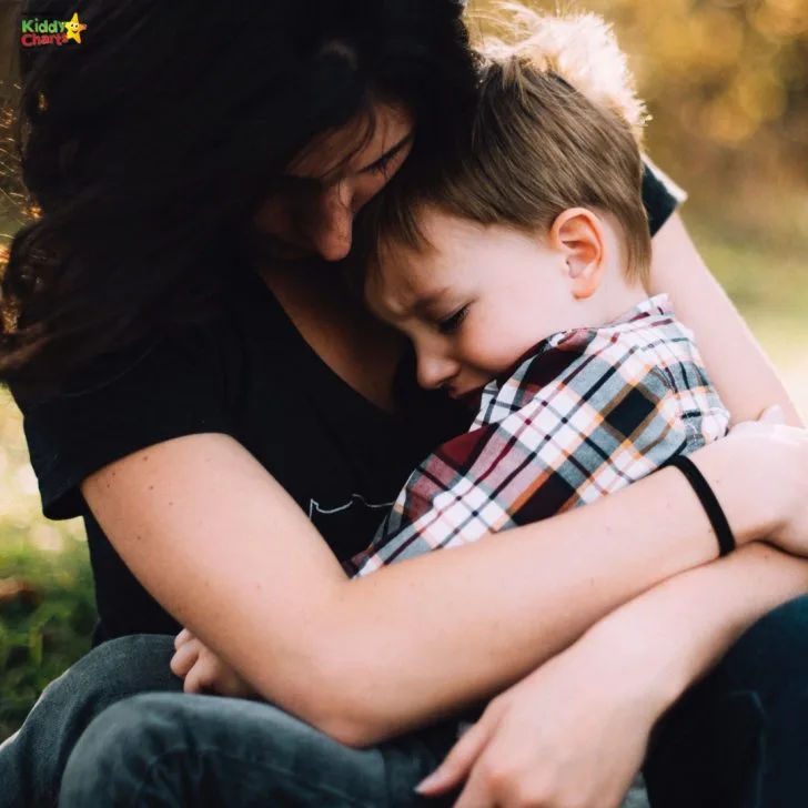 A person and their loved one are sitting outdoors, embracing in a hug and sharing a loving kiss.