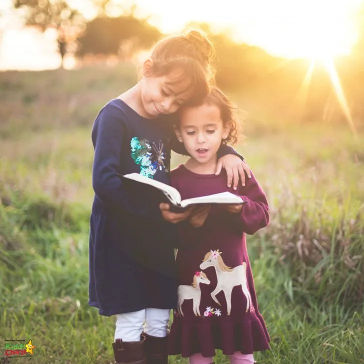 A young person with a toddler in a field of grass is smiling and enjoying the outdoors.