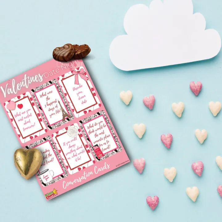 A heart-shaped Valentine's Day card is surrounded by conversation cards, charts, and other decorations, creating a romantic atmosphere for a special date night.