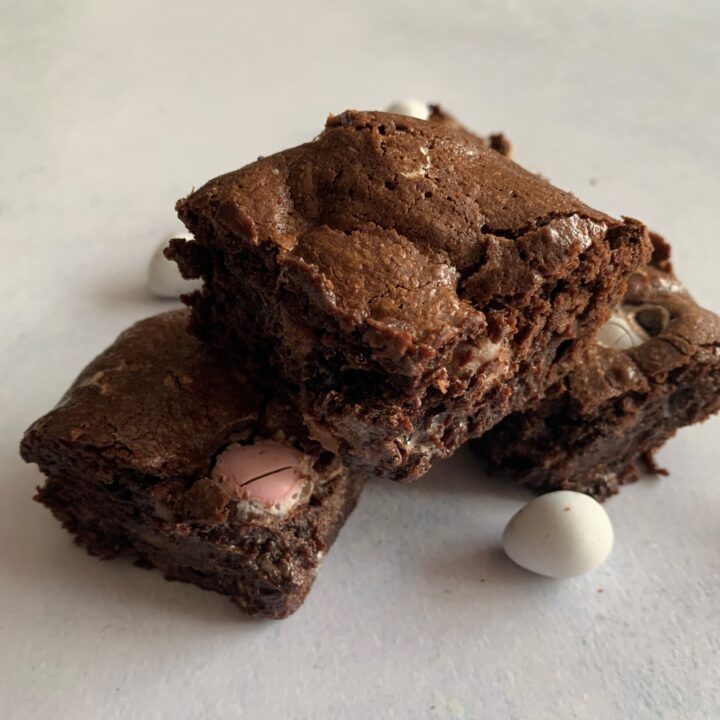 A freshly-baked chocolate brownie, sprinkled with cocoa solids and confectionery, sits invitingly on a plate, ready to be enjoyed as a delicious snack or dessert.