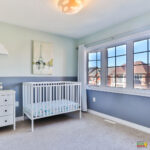 A cozy bedroom with a bed, chest of drawers, nightstand, infant bed, cabinetry, and furniture is illuminated by the natural light coming through the window, creating a warm and inviting atmosphere for the nursery.