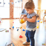A young person and toddler play together with a ball and toy indoors, their happy faces illuminated by the warm light.