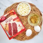 A box of Betty Crocker Delights Super Moist Red Velvet Cake Mix sits on a winter-themed table, inviting snackers to enjoy its 160 calories per package.