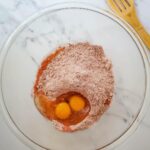 A yellow egg-shaped dessert sprinkled with powdered sugar is served on a plate indoors.