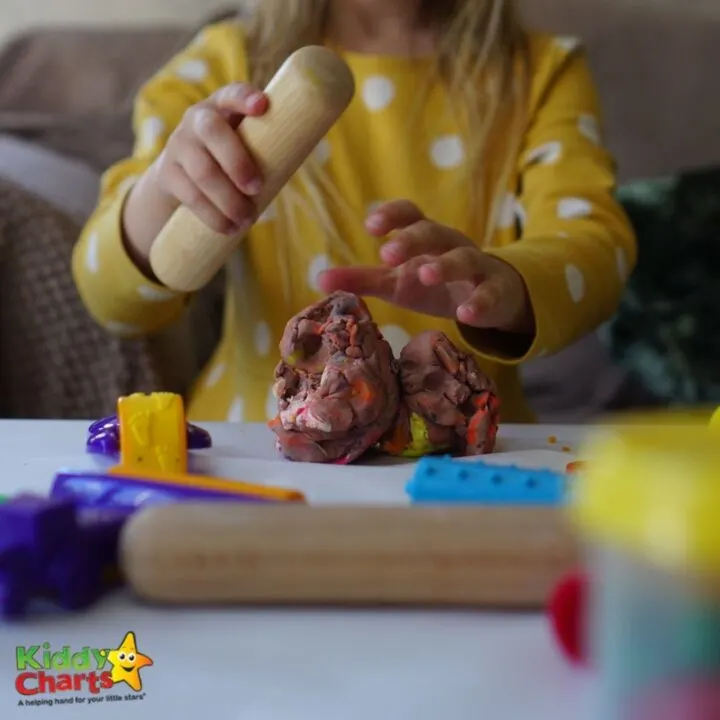 A smiling child holds a toy in one hand and a plate of food in the other while sitting indoors.