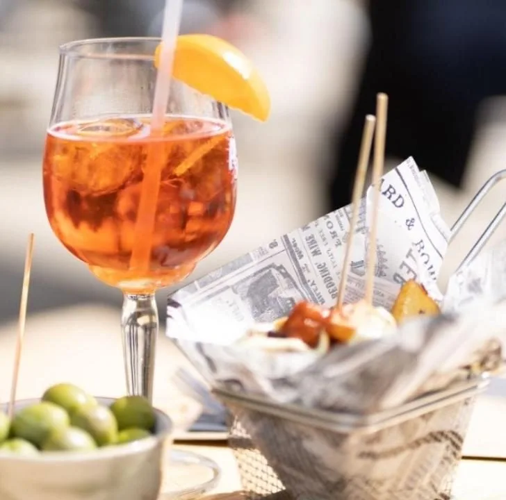 A classic cocktail is being prepared on a table filled with barware, tableware, drinkware, kitchen utensils, aperitif, juice, and a cocktail garnish, all served in an old fashioned glass.
