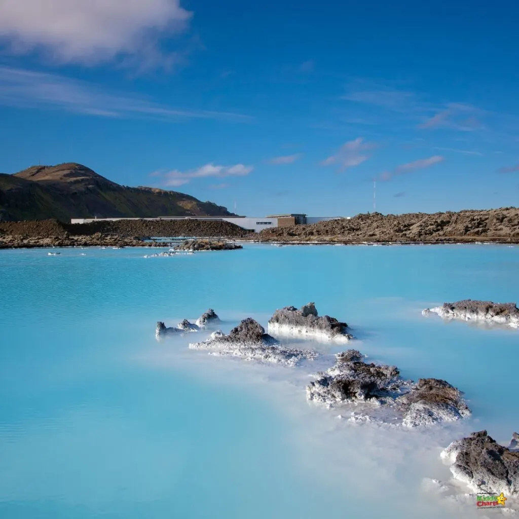 The Blue Lagoon sits in the backdrop of a landscape featuring rocks and land.