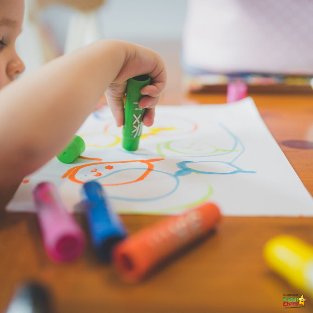 A toddler is using a marker and crayon to create art with office supplies on a Kiddy Chart in an indoor office setting.