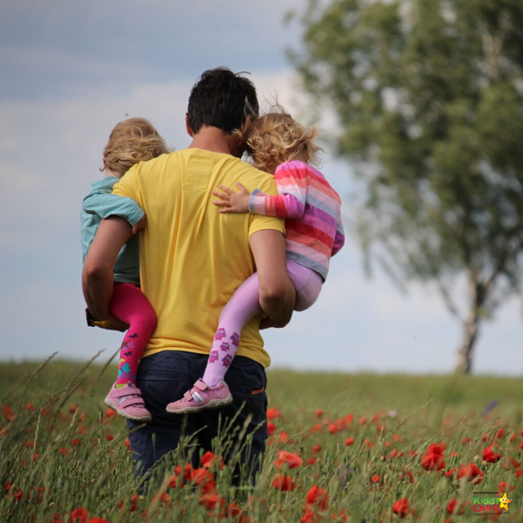 A toddler stands in a field of coquelicot flowers, holding a plant in their hand and looking up at the sky.
