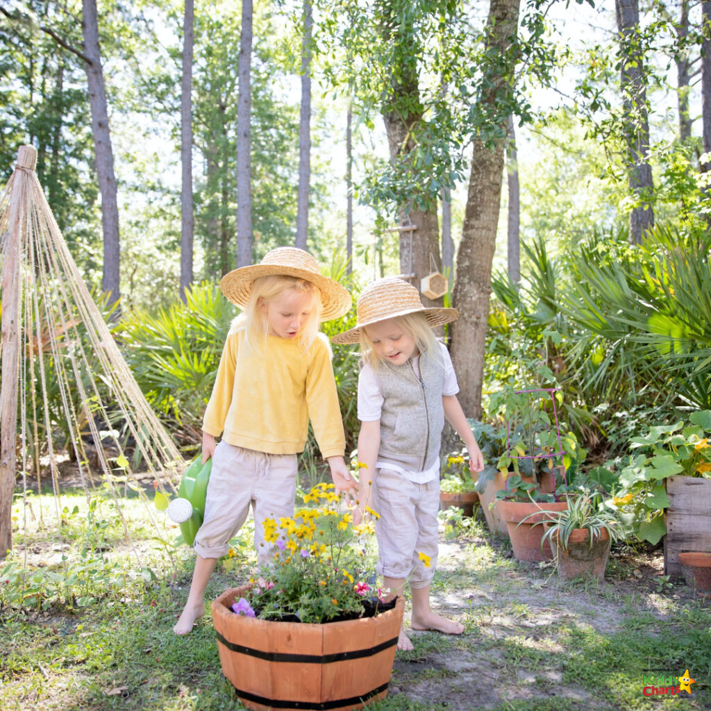 A person wearing a sun hat stands in a garden surrounded by a tree, a flowerpot, wood, and plants with flowers.
