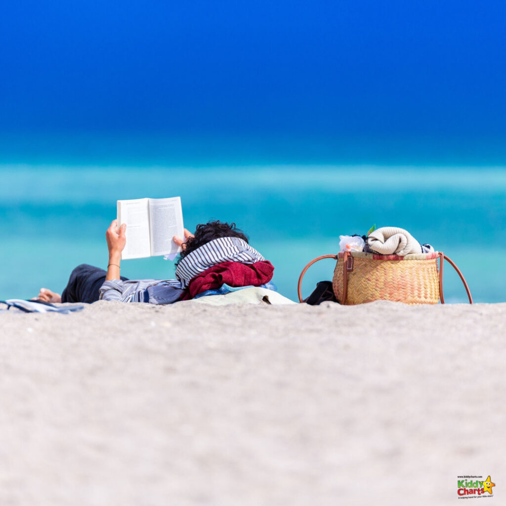 A person lies on the beach reading a book.