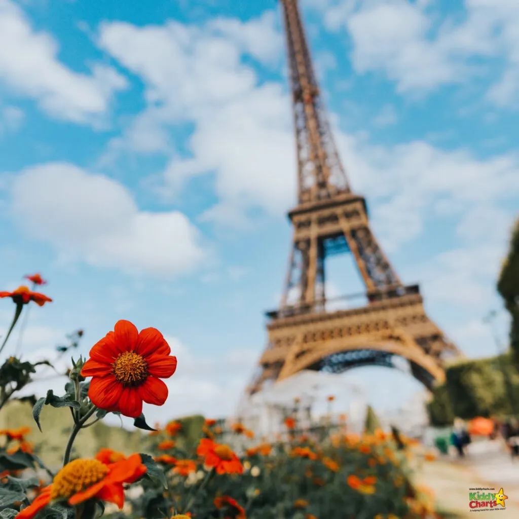 The sky is dotted with fluffy clouds, while a tall red tower stands amidst a vibrant outdoor garden of colorful flowers and lush plants.