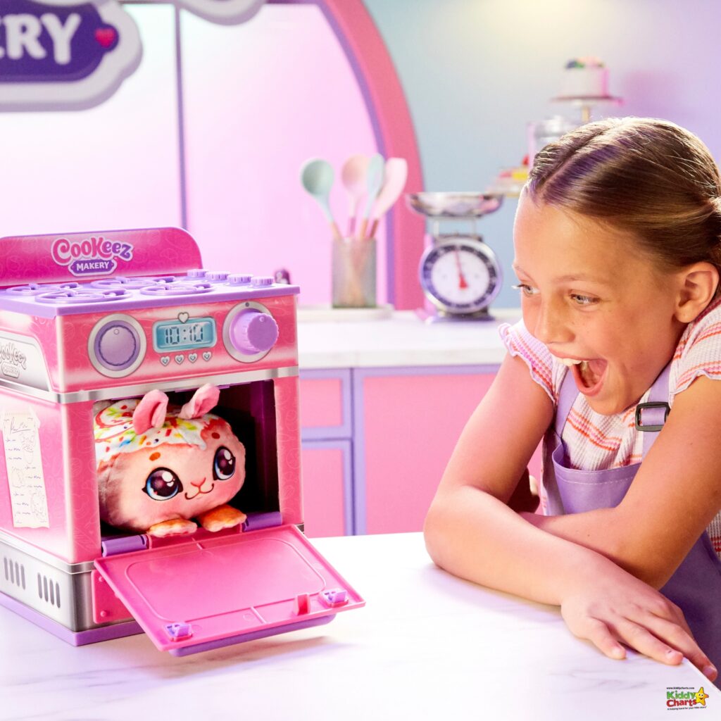 A child is excitedly looking at a toy oven with a cute plush toy inside. The background features a kitchen playset with pastel colors.