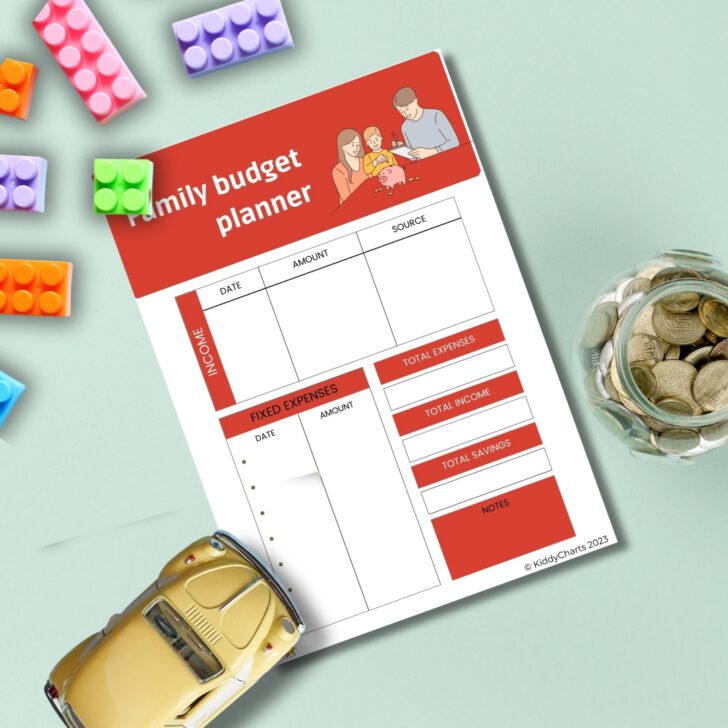 A family budget planner is surrounded by colorful toy blocks, a small toy car, and a glass jar filled with coins, suggesting financial planning and family savings.
