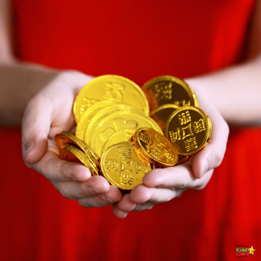 The image shows a person holding a collection of shiny golden coins in open hands, with a blurred red background enhancing the coins' brightness.