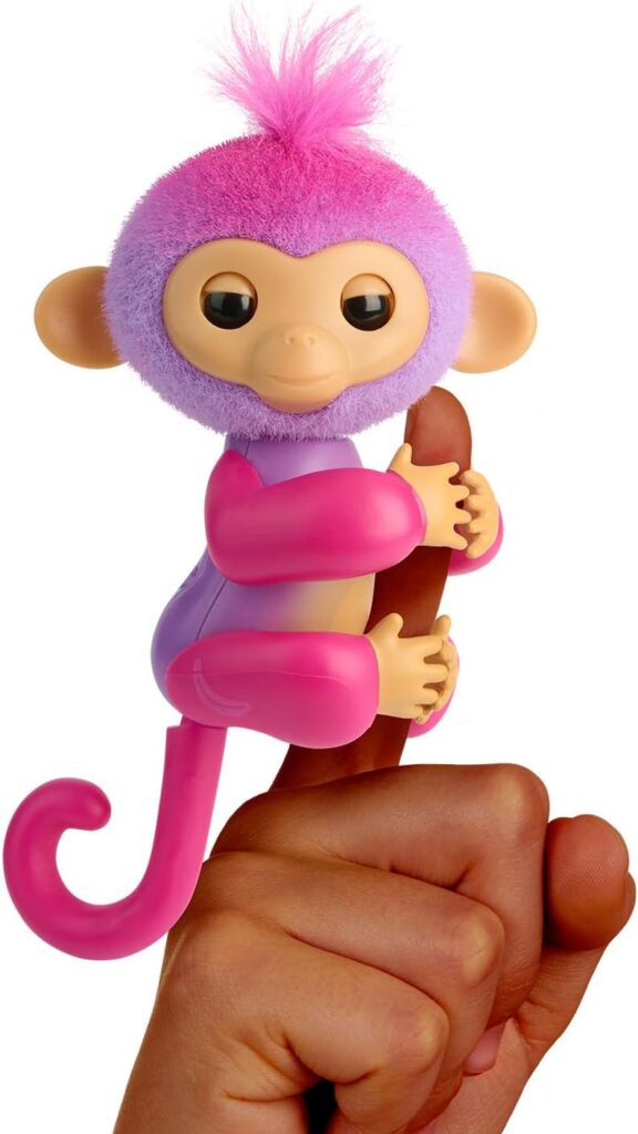This is an image of a colorful plastic toy monkey with pink and purple fur holding onto a human finger with its limbs and tail.
