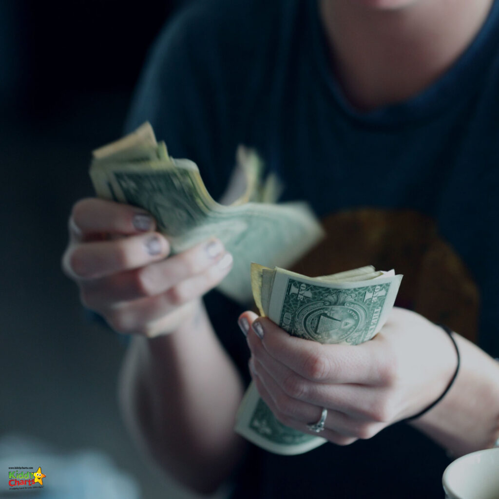 A person is counting a handful of US dollar bills. The focus is on the money, with a blurred background and a partial view of the person.