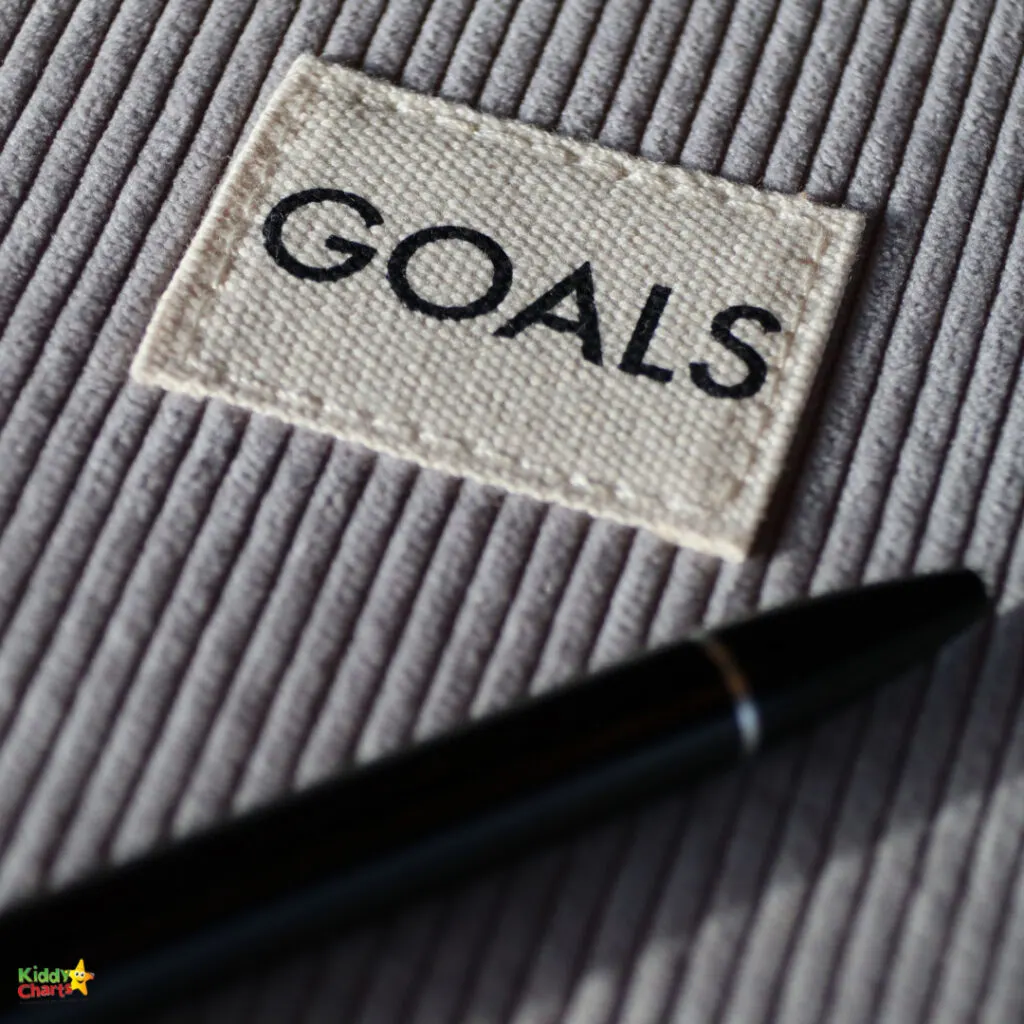 A fabric label with the word "GOALS" rests on a ribbed surface next to a black pen, symbolizing planning, objectives, or resolutions.