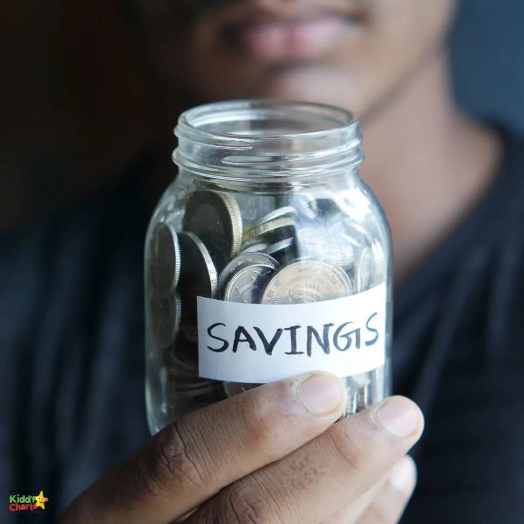 A person holds a clear jar filled with coins labeled "SAVINGS." The focus is on the jar, with the individual's face partially visible, blurred in the background.