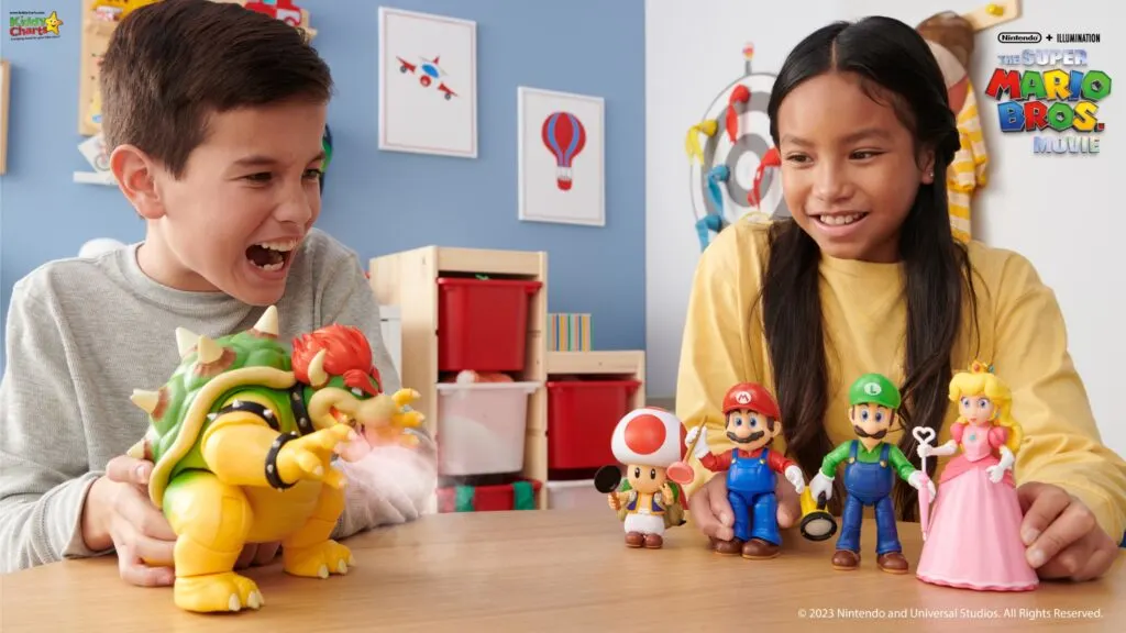 Two kids are joyfully playing with Super Mario character toys on a table in a room decorated with kid-friendly wall art.
