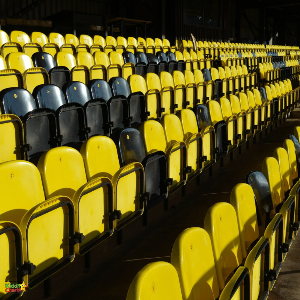 Empty yellow and black stadium seats in sunlight with shadows, creating a pattern in a sports arena, with no people visible.