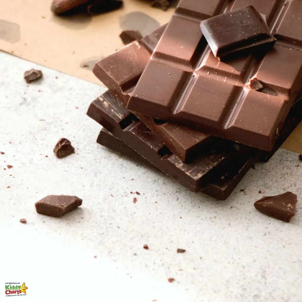 The image shows stacked pieces of dark brown chocolate on a light surface scattered with small chocolate fragments, suggesting a rich, indulgent treat.