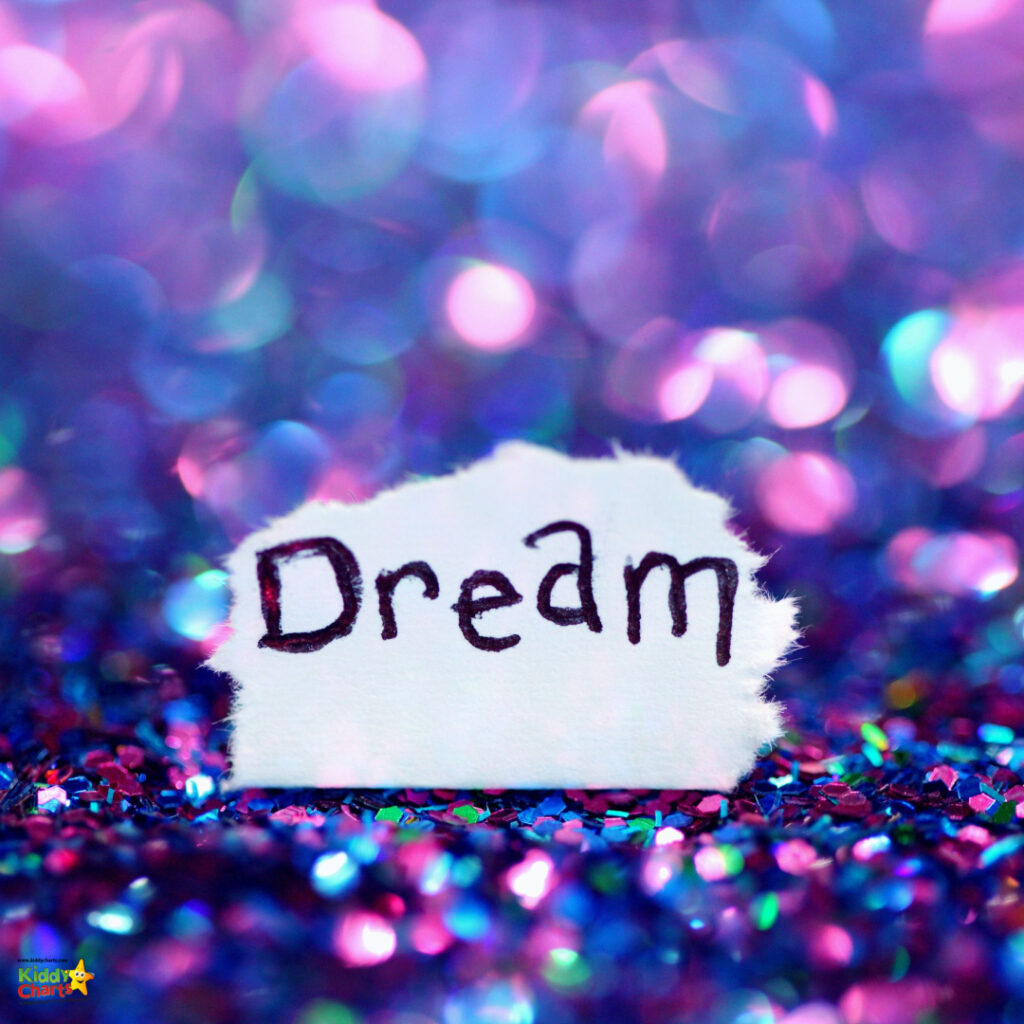 A piece of torn white paper with the word "Dream" handwritten on it, set against a shimmering, multicolored glitter background.