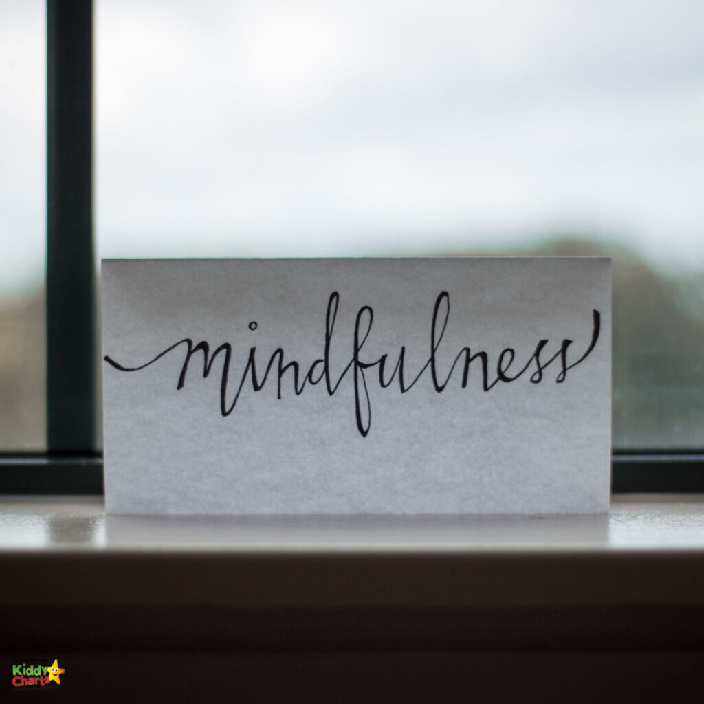 A piece of paper with "mindfulness" written in cursive stands on a windowsill, with a blurred background suggesting a natural outdoor setting.