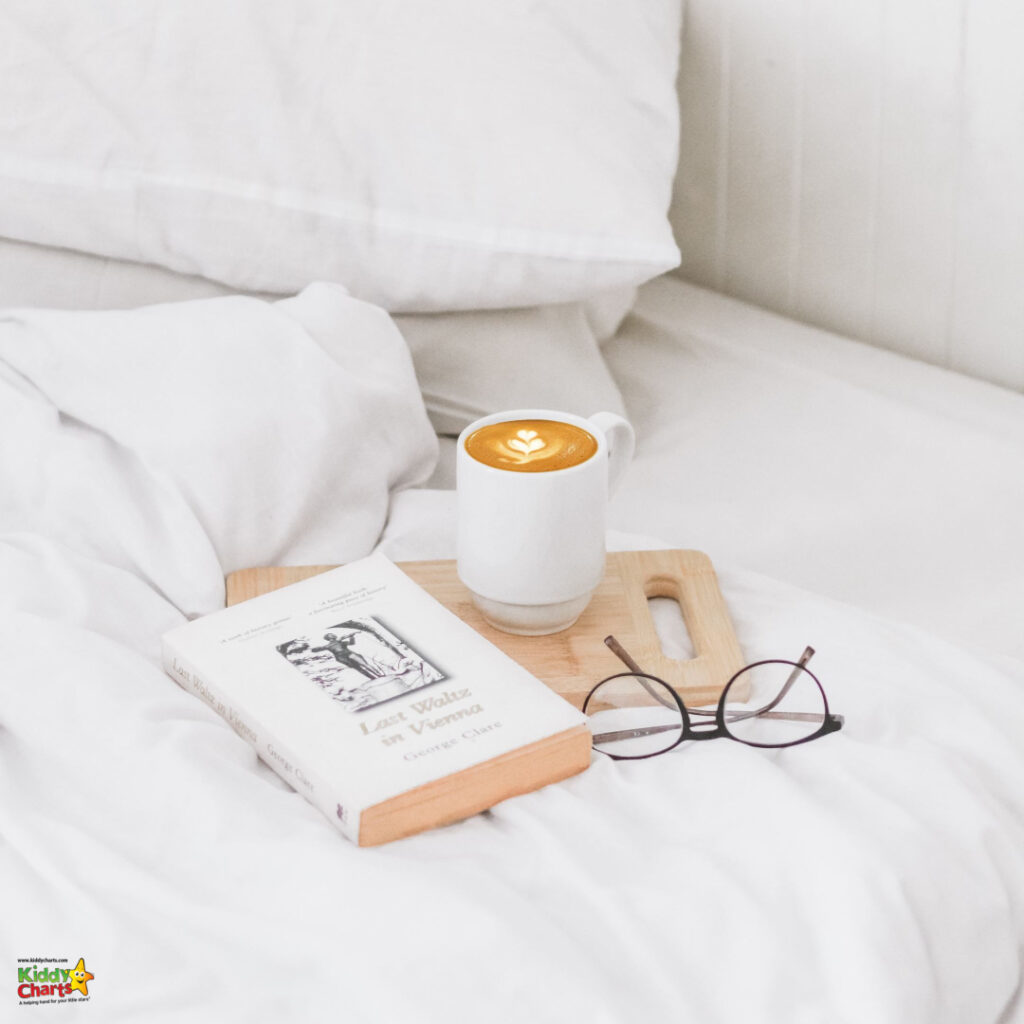 A cozy setting with a book titled "Last Year I was Vanessa" and glasses on a bed, beside a cup of coffee with artful foam on a wooden tray.