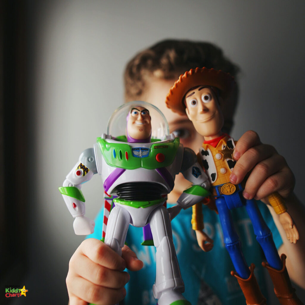 A person holds up Buzz Lightyear and Woody action figures, with a partial view of their face in the background, focused on the toys.