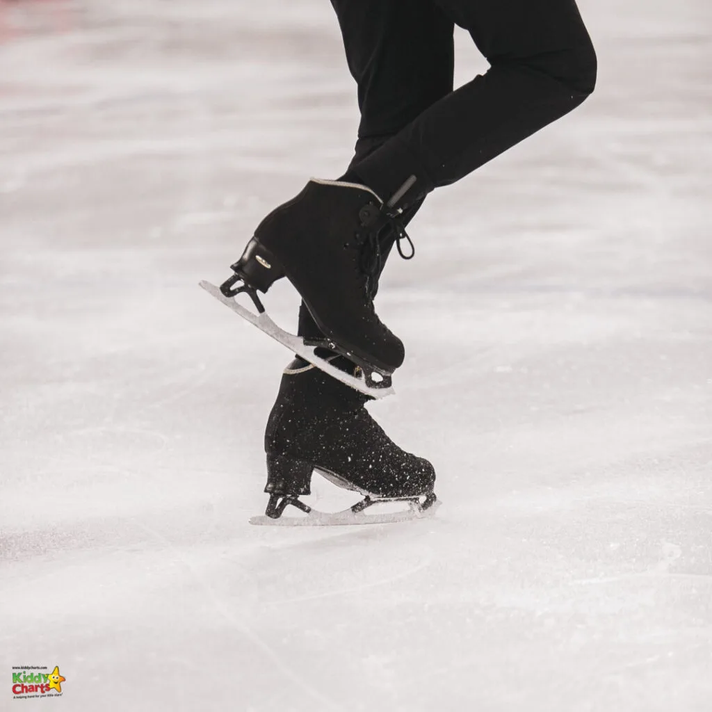Close-up of a person's legs wearing black ice skates on an ice rink, captured mid-motion with ice shavings visible around the blade.