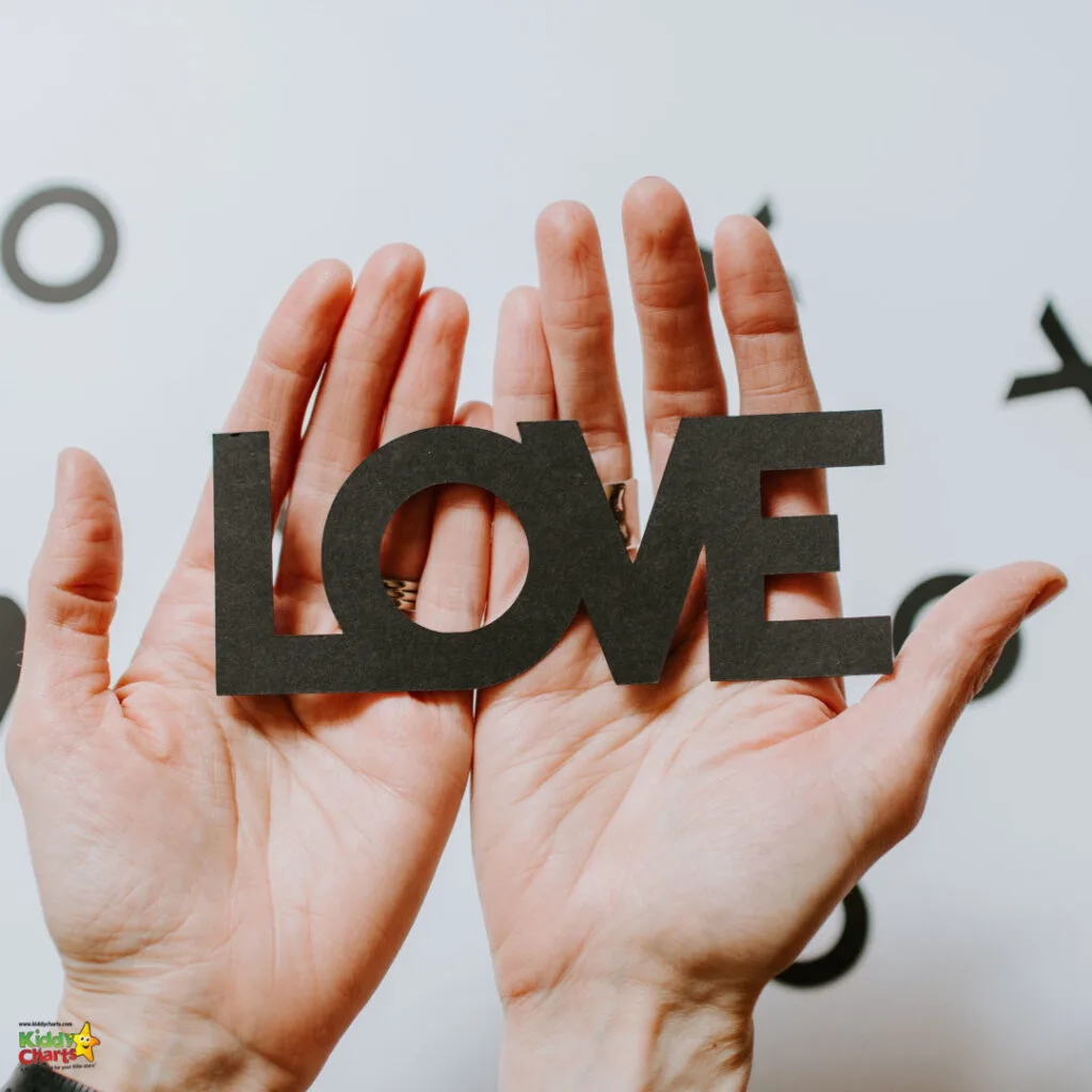 A person holds up the word "LOVE" written in black capital letters, against a white background with whimsical, black wall decals.