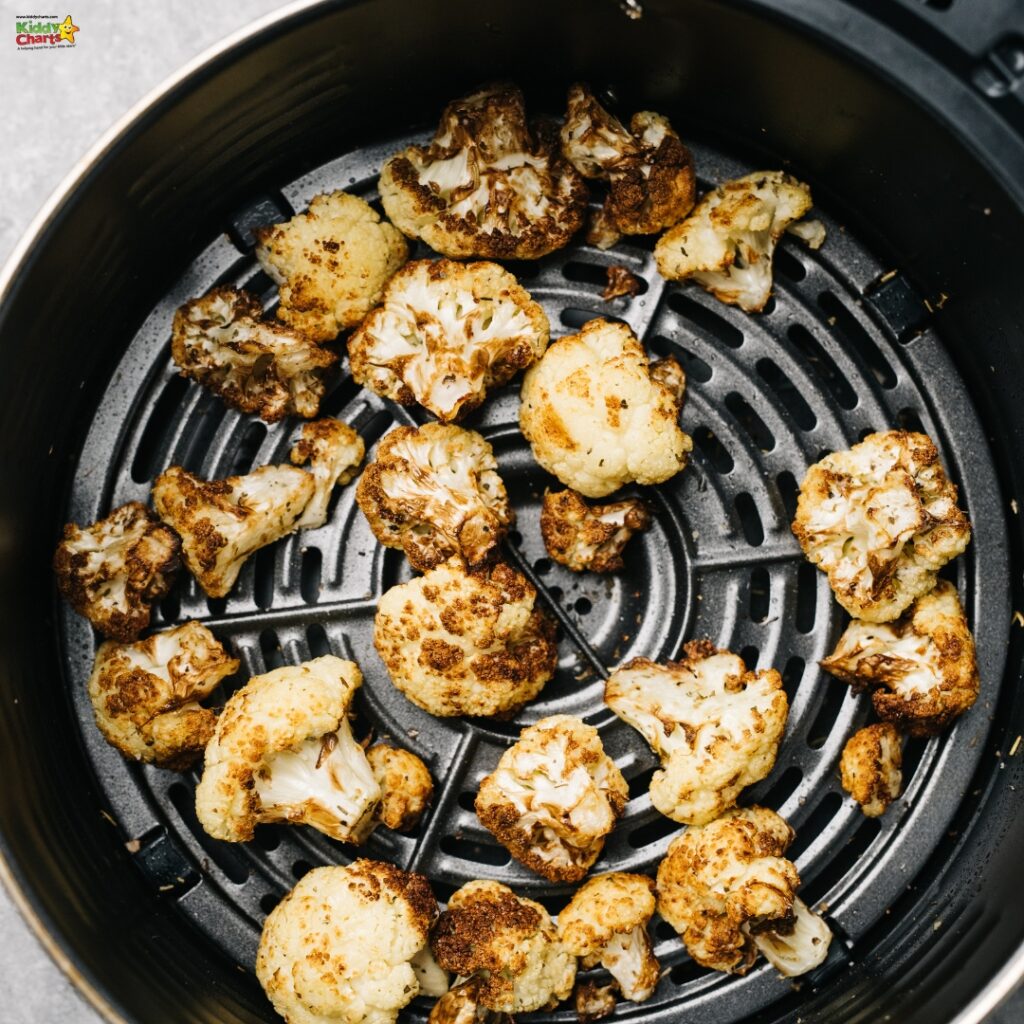 Roasted cauliflower florets inside an air fryer basket, showing crispy edges and golden-brown color, indicating a cooked, healthy vegetable dish.