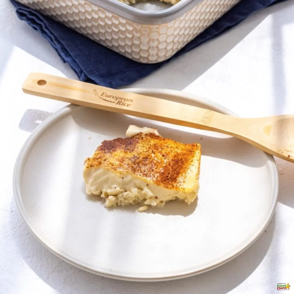 A slice of baked custard pie on a white plate with a wooden spatula labeled "European Rice," with a patterned kitchen towel and a dish in the background.