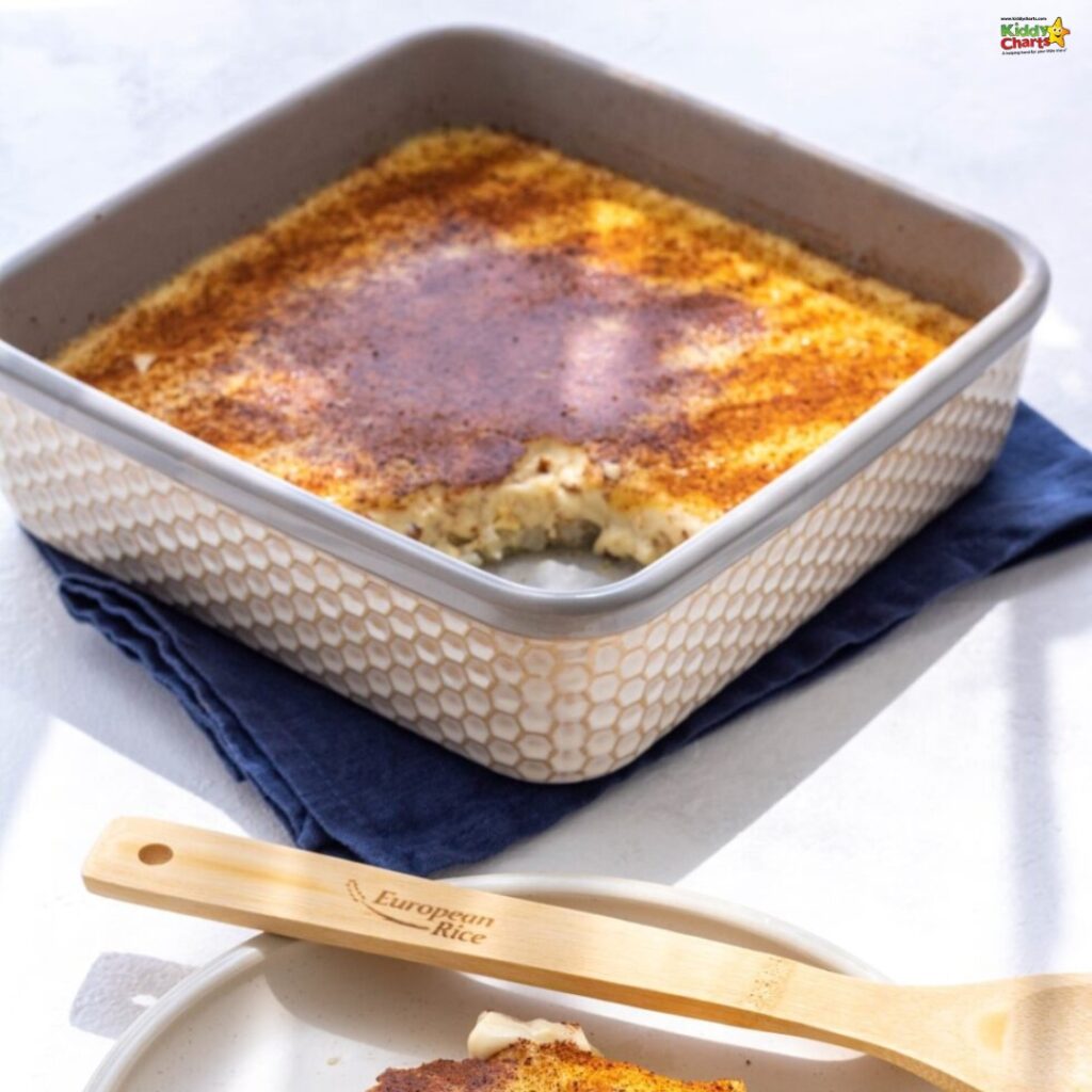 A golden-brown baked dish in a patterned square ceramic pan, sitting on a dark cloth, with a wooden spatula labeled "European Rice". Looks like a rice pudding.